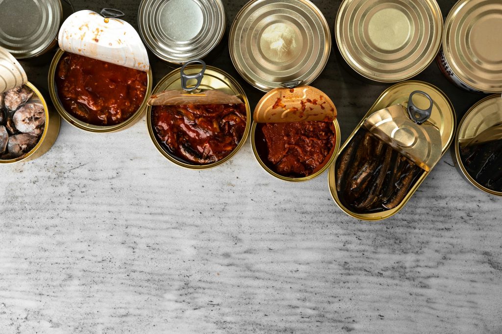 Top view of opened cans with fish conserves on wooden background