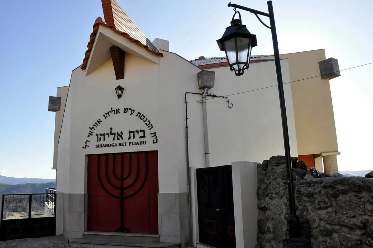חזית בית הכנסת בית אליהו בבלמונטה, עם שמו בעברית ודלת אדומה המעוטרת במנורה