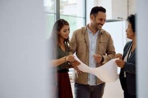 Happy couple of buyers and real estate agent analyzing housing plans.
